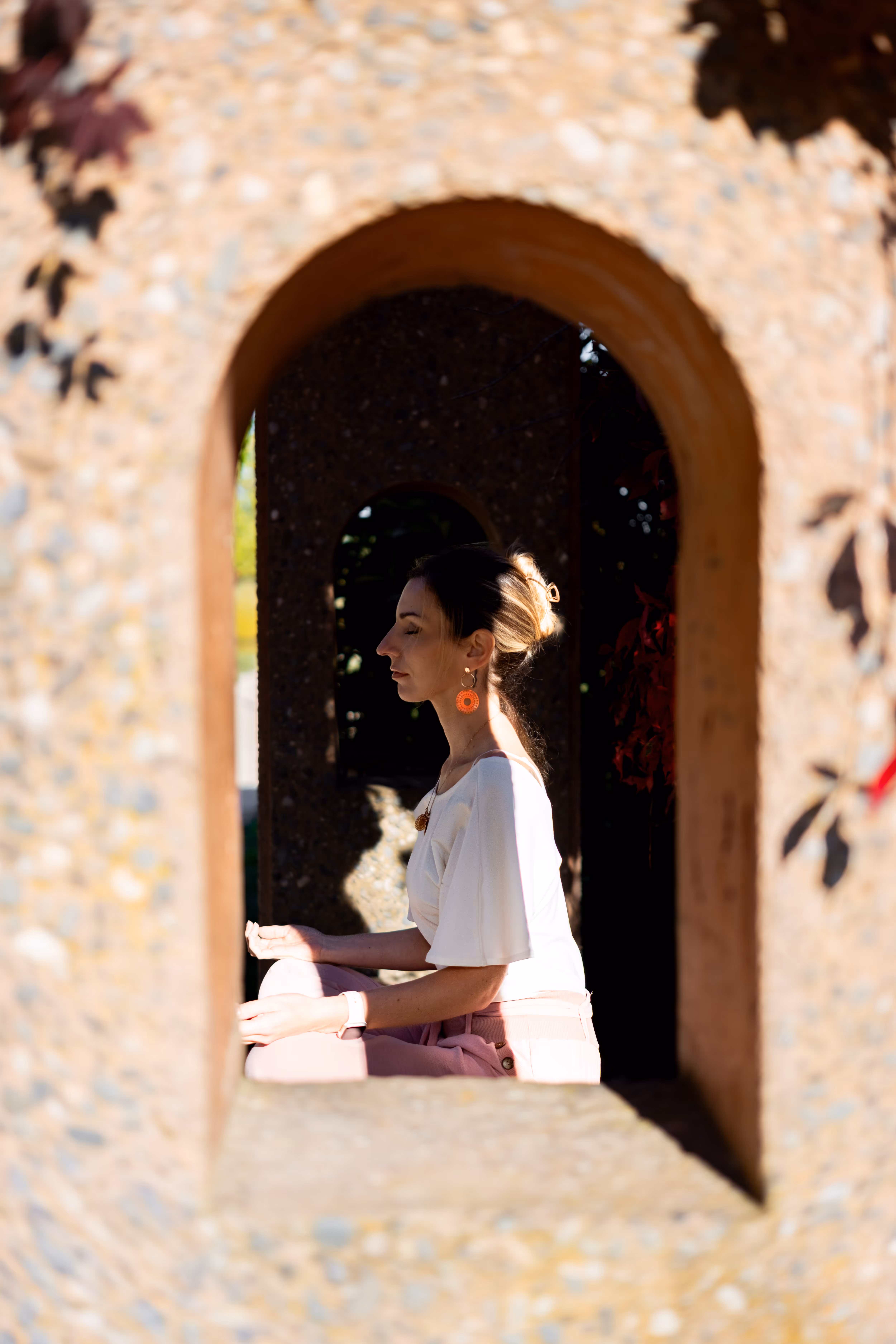 Mélissa Vidal, psychologue, pratiquant la méditation de pleine conscience en extérieur, assise en tailleur et cadrée par une arche en pierre naturelle.